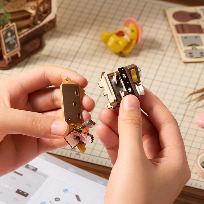 Hands holding small mechanical models on a desk with stationery items.